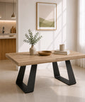 Tavolo allungabile moderno con piano effetto noce e struttura in metallo ghisa, caratterizzato da gambe geometriche a trapezio e inserito in un ambiente scandinavo luminoso con cucina a vista e ampie finestre.