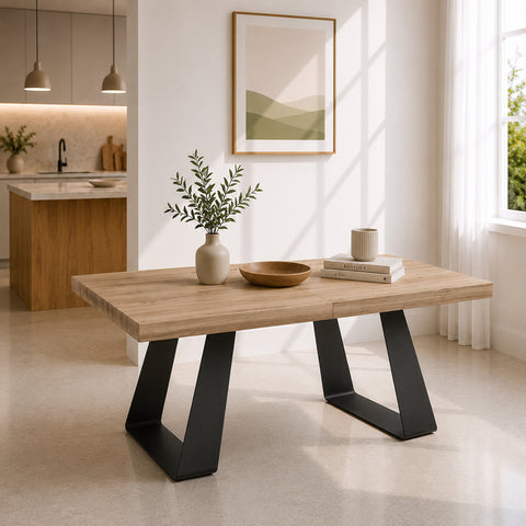 Tavolo allungabile moderno con piano effetto noce e struttura in metallo ghisa, caratterizzato da gambe geometriche a trapezio e inserito in un ambiente scandinavo luminoso con cucina a vista e ampie finestre.