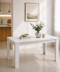 Tavolo allungabile bianco opaco con struttura lineare e gambe quadrate, inserito in un ambiente moderno e luminoso con cucina a vista, ampie finestre e arredamento minimalista