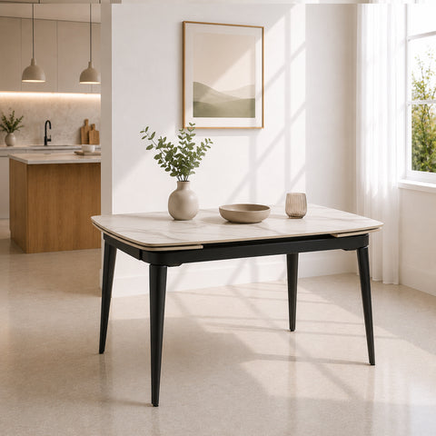 Tavolo allungabile rettangolare con angoli arrotondati, piano effetto marmo Carrara bianco e gambe effetto ghisa, inserito in un ambiente moderno e luminoso con cucina a vista e grandi finestre.