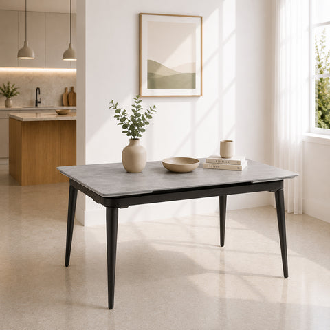 Tavolo allungabile rettangolare con angoli arrotondati, piano effetto pietra Grigia e gambe effetto ghisa, inserito in un ambiente moderno e luminoso con cucina a vista e grandi finestre.