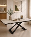 Tavolo allungabile Hidra con piano in gres ceramico effetto marmo Carrara e basamento centrale incrociato in metallo nero, ambientato in una moderna sala da pranzo.
