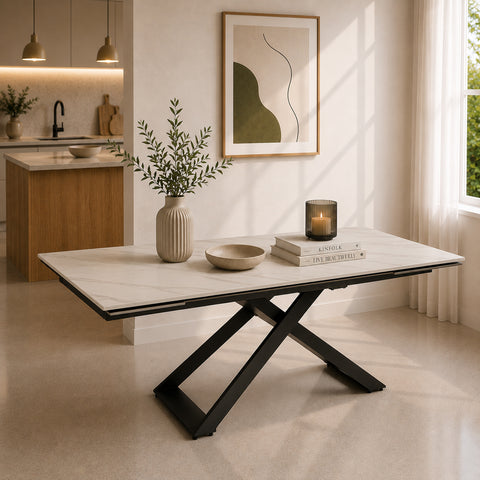 Tavolo allungabile Hidra con piano in gres ceramico effetto marmo Carrara e basamento centrale incrociato in metallo nero, ambientato in una moderna sala da pranzo.
